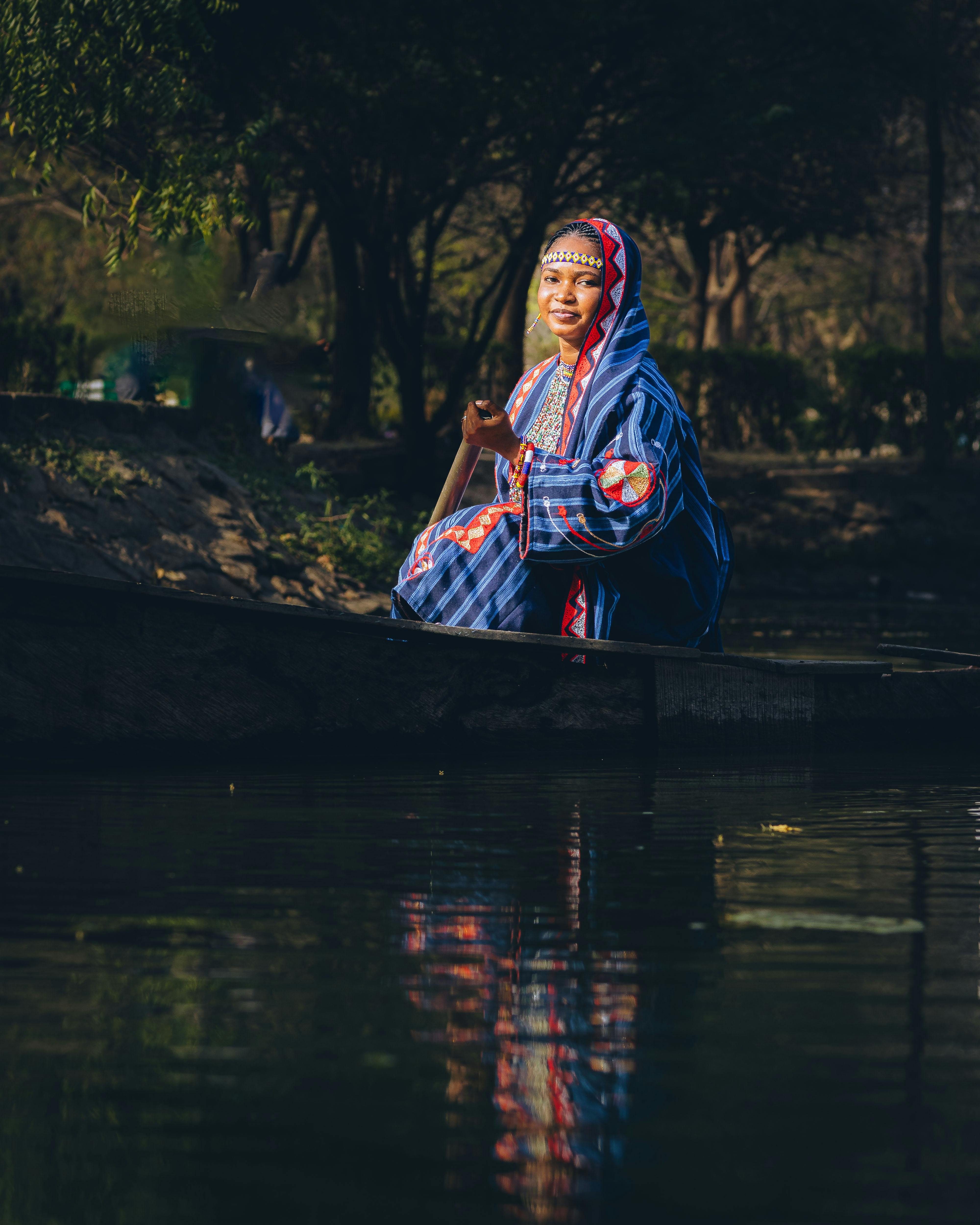 ฟรี หญิงในชุดพื้นเมืองไนจีเรียพายเรือแคนูในแม่น้ำที่สงบนิ่ง คลังภาพถ่าย
