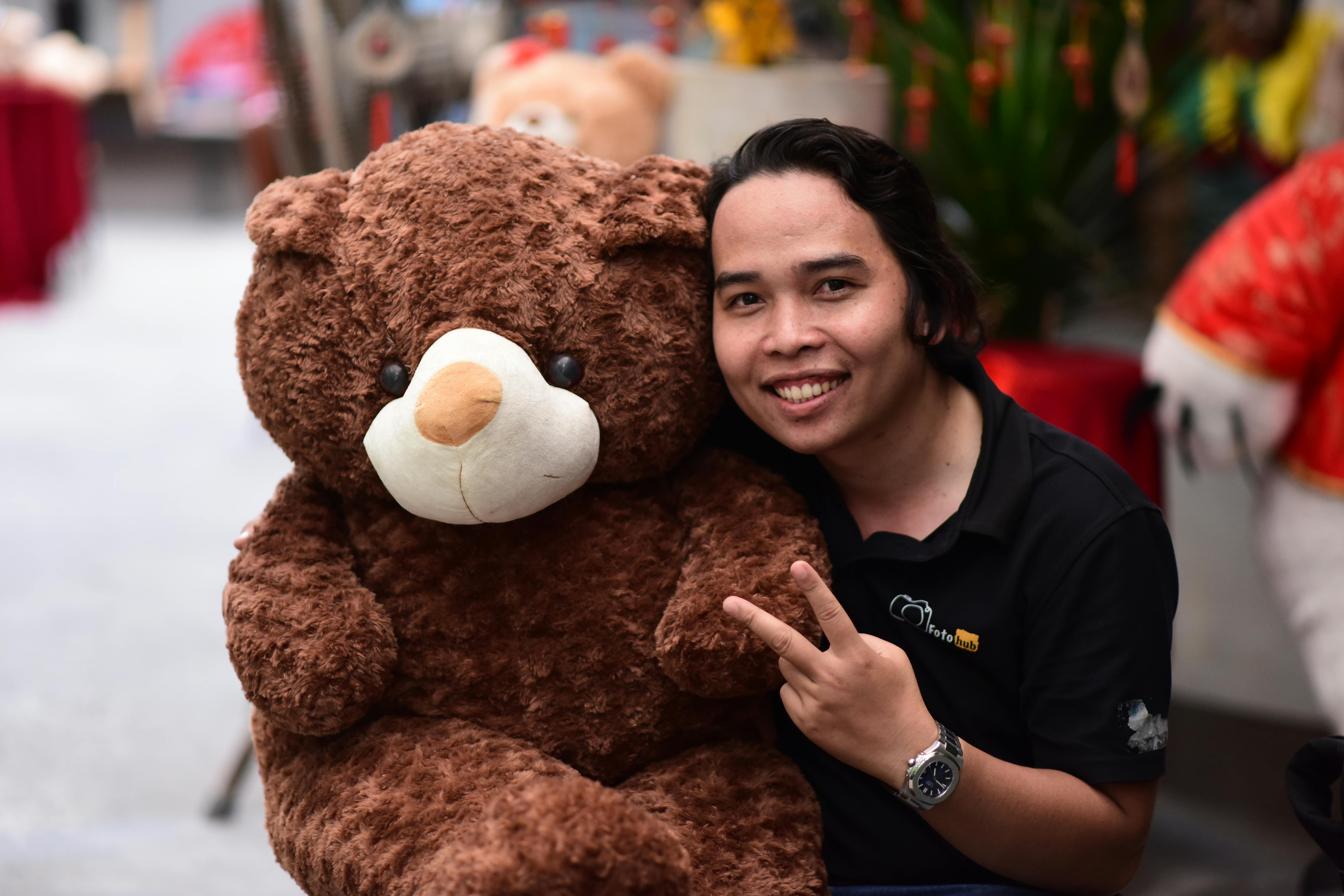 A cheerful man in a black polo shirt posing with a large brown teddy bear indoors. Perfect for lifestyle themes.