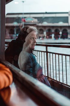 Man gazing pensively through ferry window, reflection highlighting introspection.