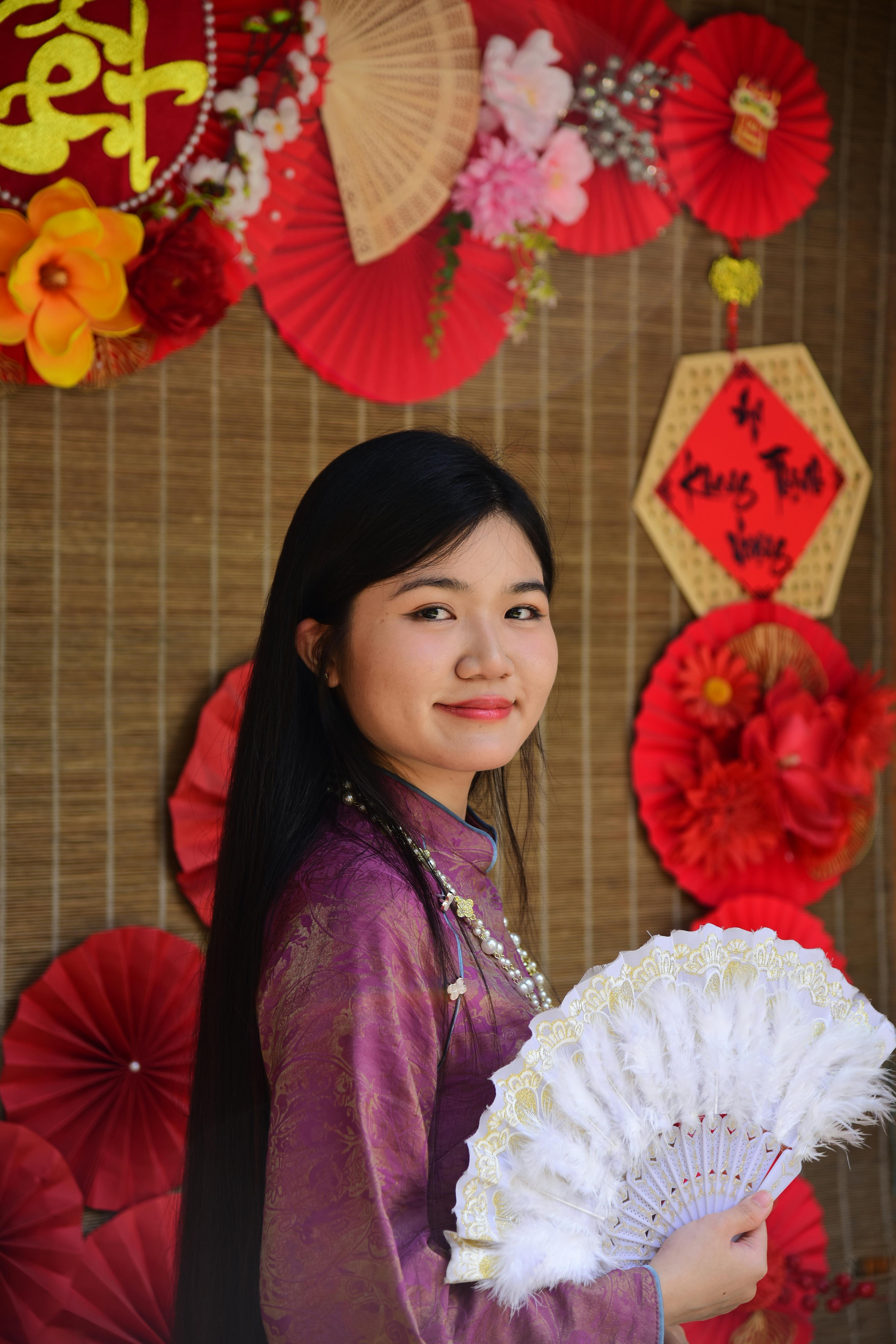 ฟรี หญิงสาวในชุดพื้นเมืองถือพัดในระหว่างการเฉลิมฉลองเทศกาลตรุษจีน โดยมีฉากหลังตกแต่งสวยงาม คลังภาพถ่าย
