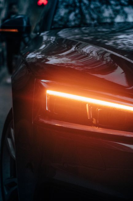 Dark and moody close-up of a car headlight at night, showcasing sleek design with reflections.