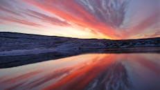 冰岛韦斯特峡湾的日落令人惊叹，宁静的湖水倒映着充满活力的天空