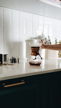 A hand brewing coffee with a Chemex on a sleek kitchen countertop, perfect for coffee enthusiasts.