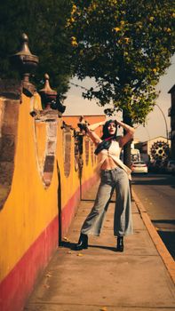 Fashionable woman posing on a sunlit street with a colorful background.
