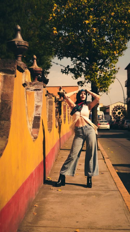 Free Fashionable woman posing on a sunlit street with a colorful background. Stock Photo