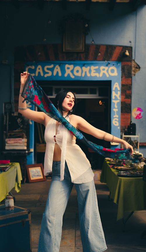 Free A woman stands confidently outside Casa Romero Antiques, holding a vibrant scarf in an artistic pose. Stock Photo