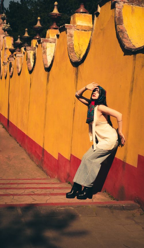 Free Stylish woman posing in urban fashion against an ornate yellow wall under the sun. Stock Photo