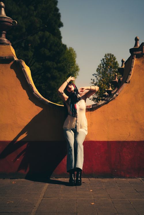 Free Chic woman poses against colorful wall in urban setting, embracing sunny day. Stock Photo