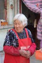 Elderly Woman in Red Apron Outside House