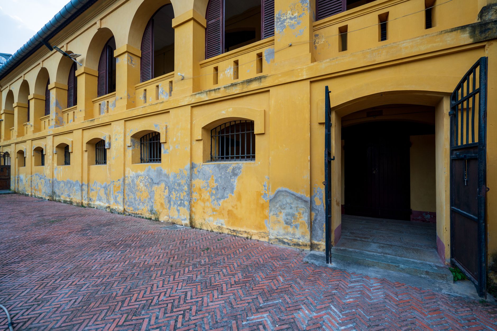 Old yellow brick building with arches and an open gate, showcasing historic architecture.