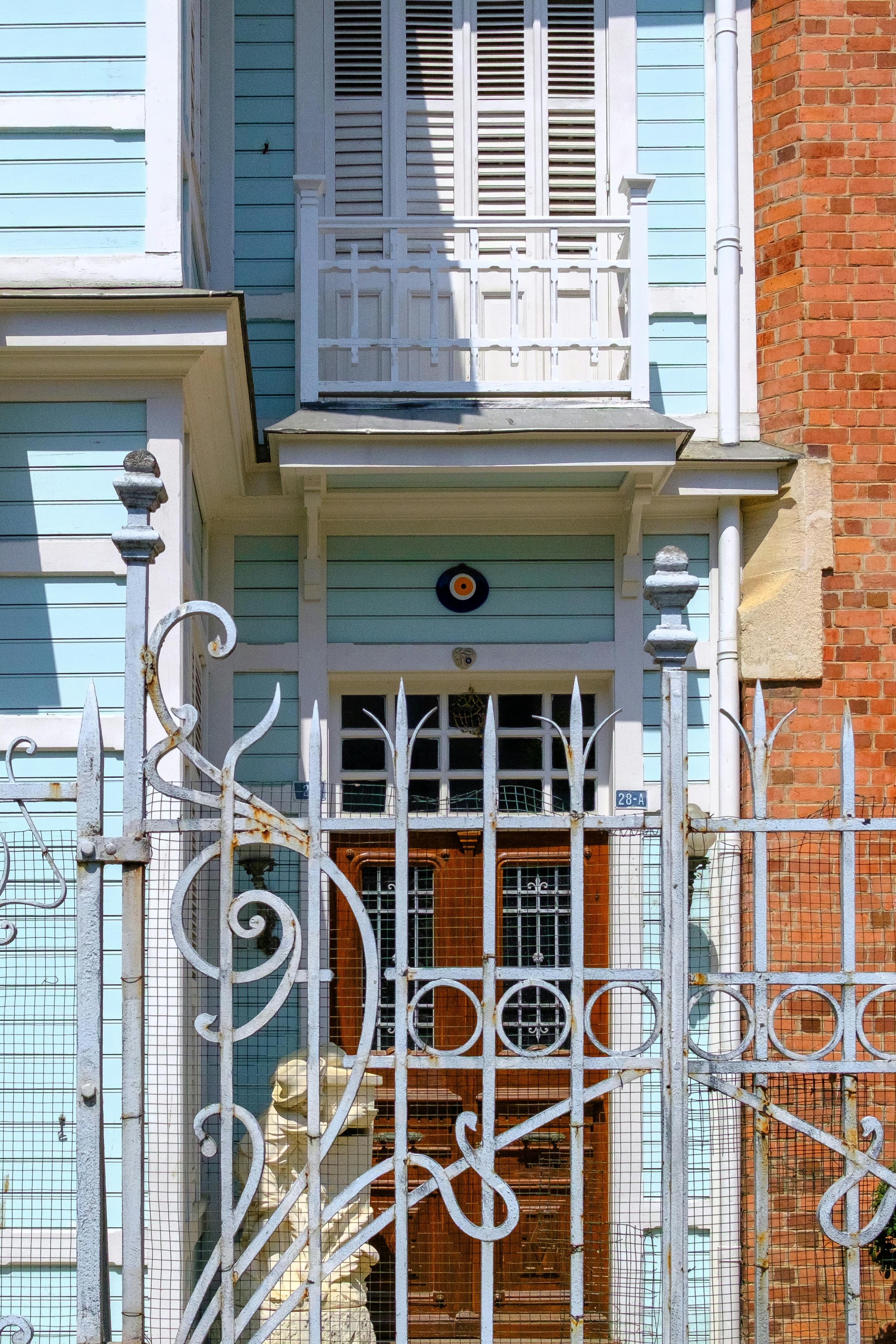 bezplatná Okouzlující průčelí domu s modrým obložením a kovanou železnou bránou za jasného slunce. Základová fotografie
