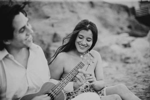 Um casal feliz desfruta de música na praia, retratado em uma fotografia em preto e branco.