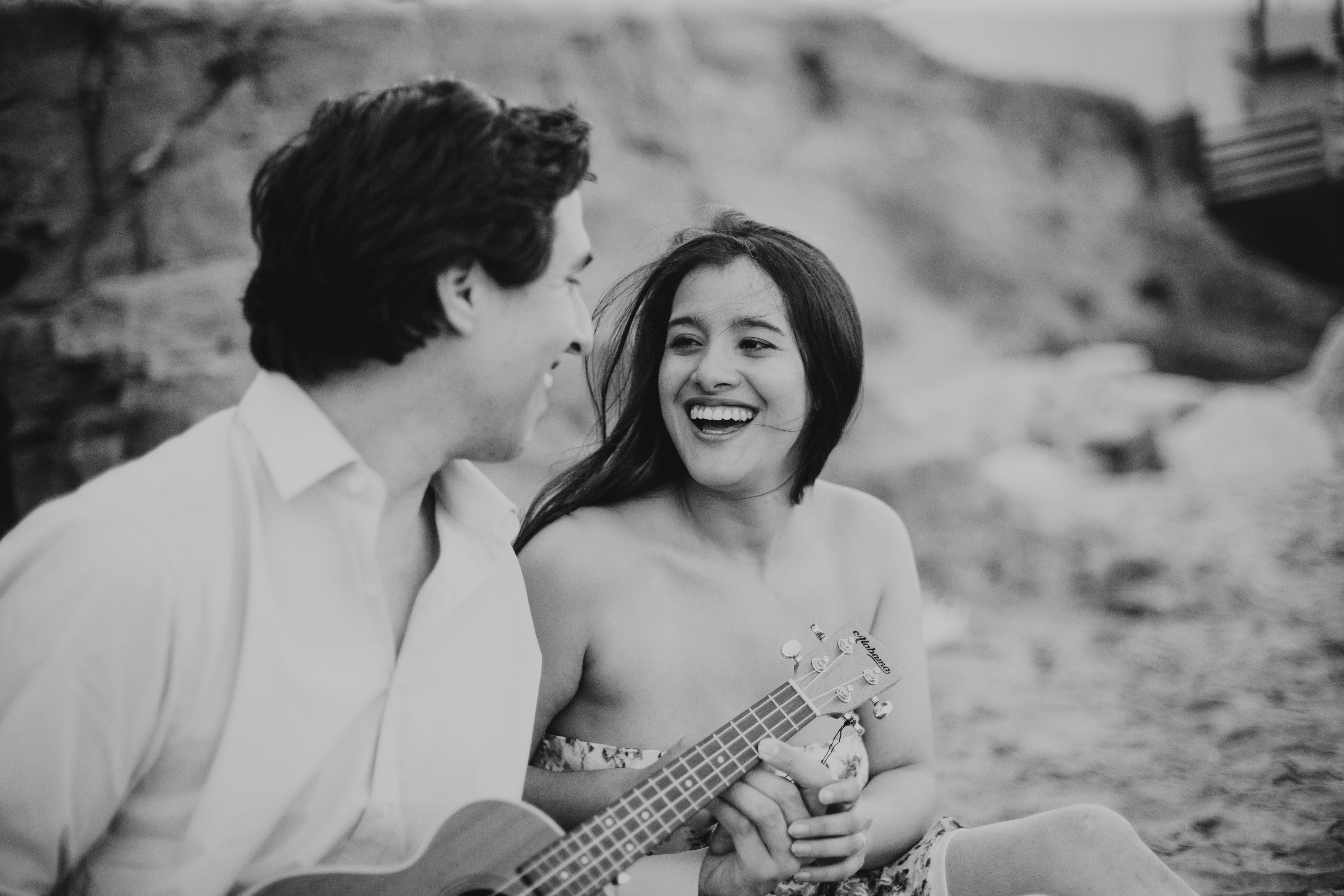 ฟรี คู่รักอารมณ์ดีนั่งอยู่บนชายหาด แบ่งปันช่วงเวลาแห่งความสุขด้วยการเล่นอูคูเลเล่ คลังภาพถ่าย