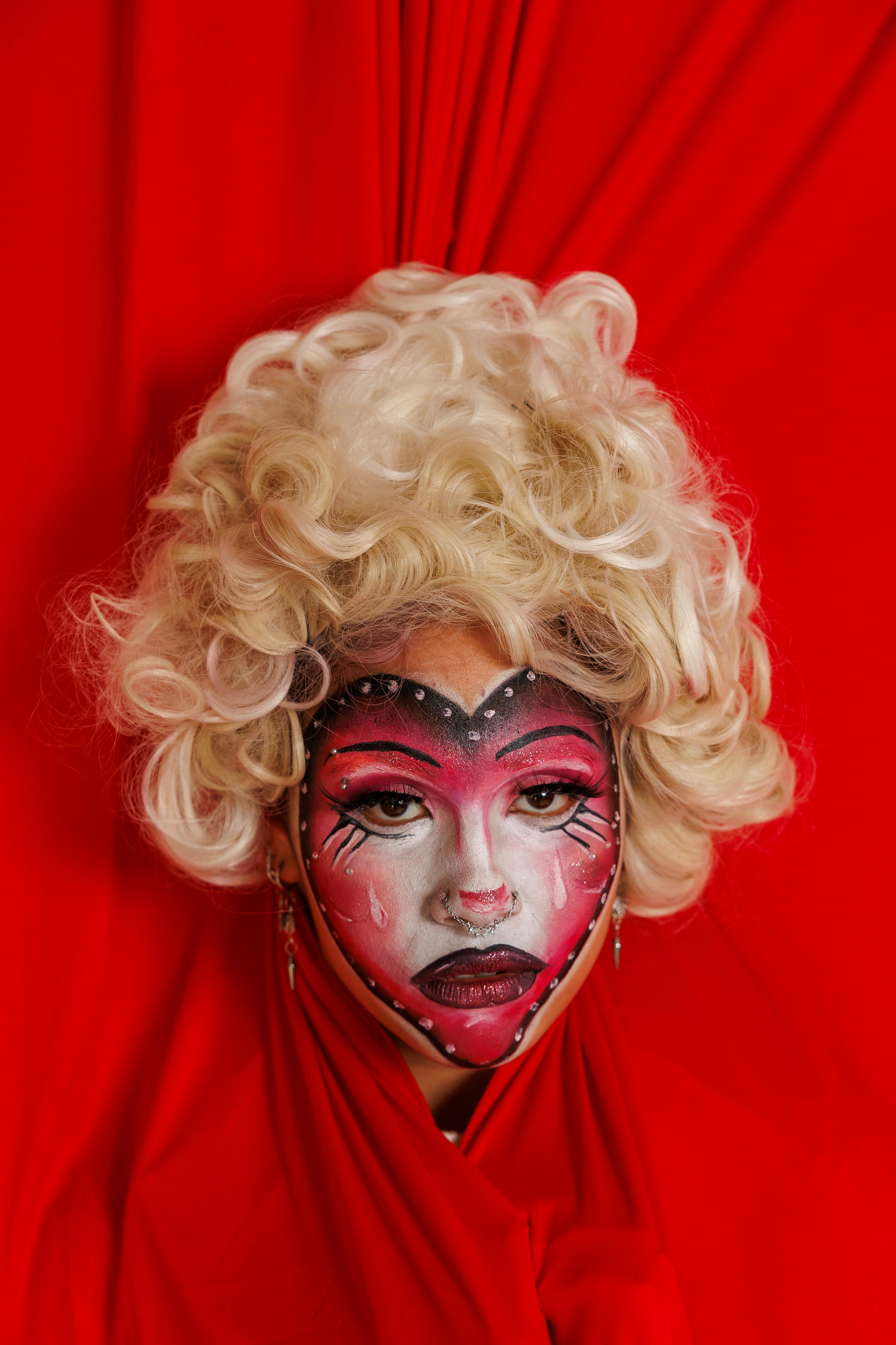 Ücretsiz Detaylı yüz boyaması ve canlı kırmızı arka planı ile sanatsal ifadeyi yakalayan çarpıcı bir yaratıcı portre. Stok Fotoğraflar