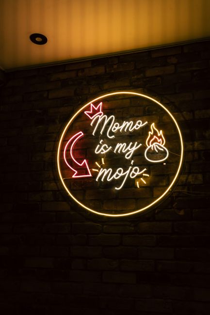 Neon sign reading 'Momo is my mojo' with warm glow, set against a brick wall.