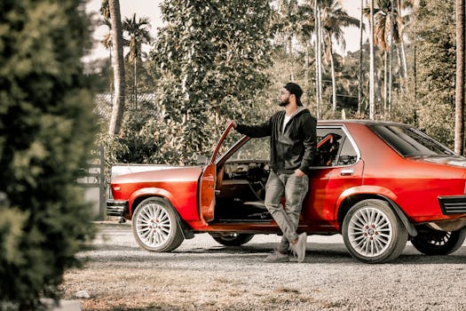 Man leaning against a classic red car outdoors, capturing a vintage automotive lifestyle.