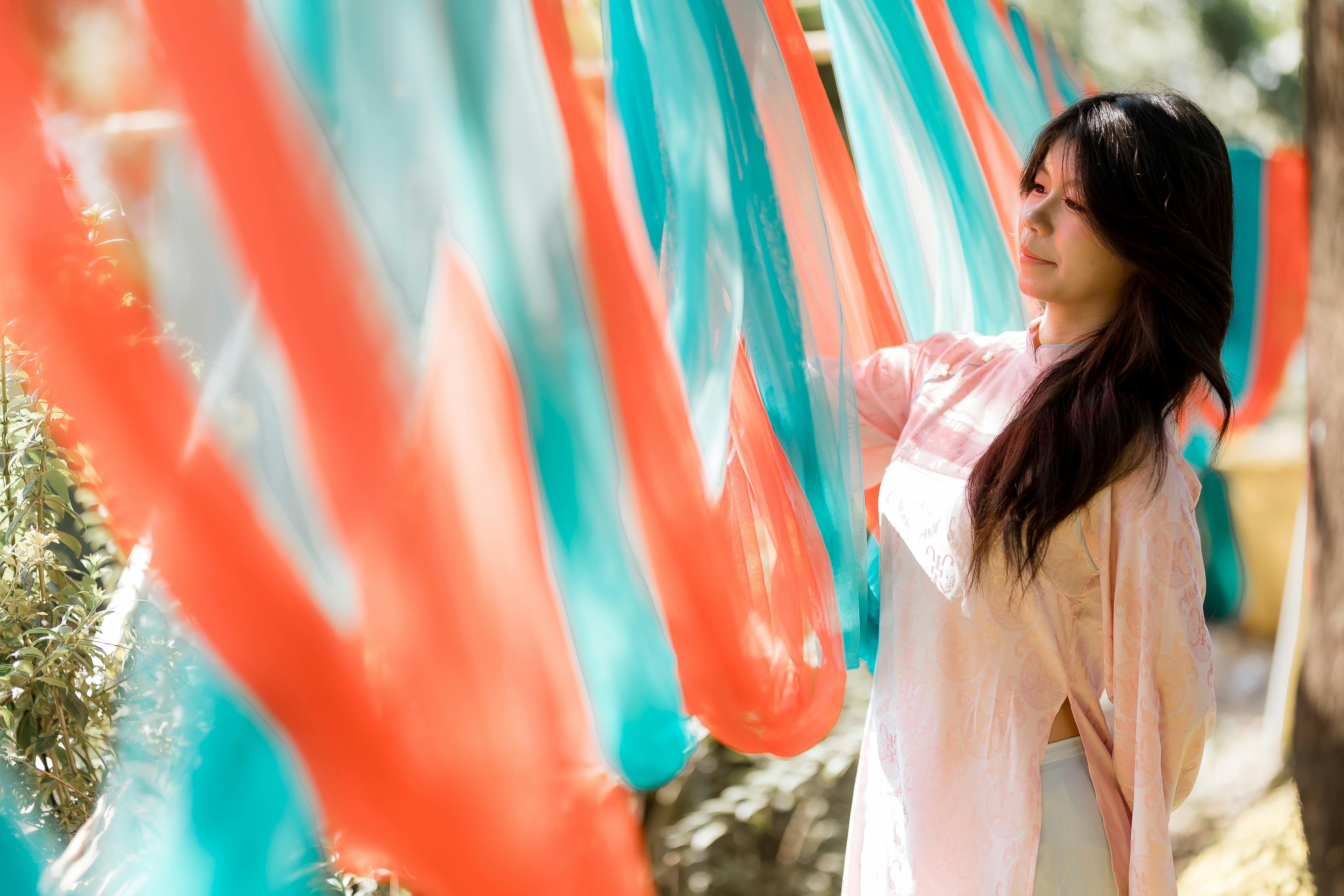 Gratis Una donna in abiti tradizionali ammira tessuti colorati in un ambiente soleggiato all'aperto. Foto a disposizione