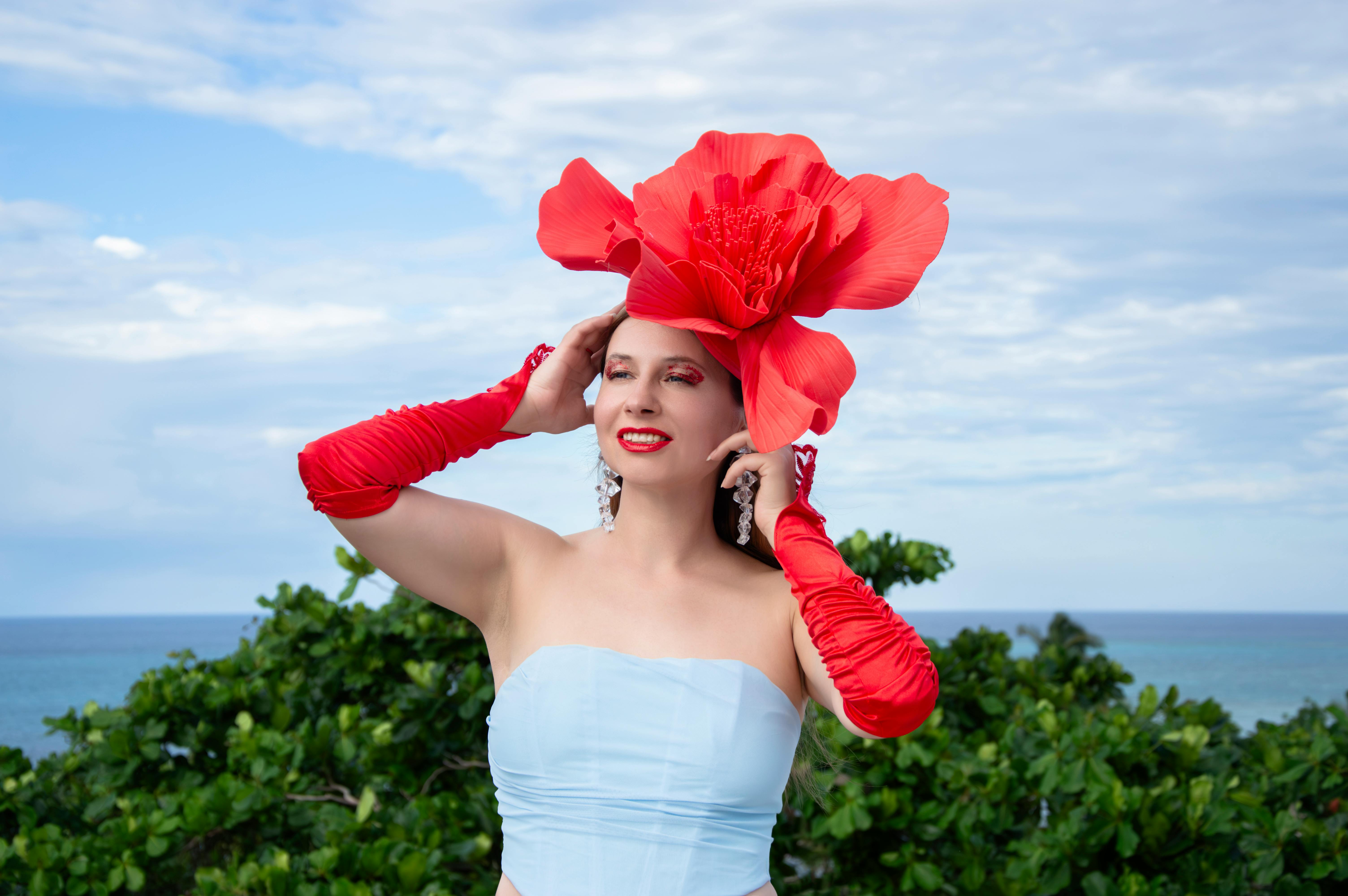 ฟรี หญิงสาวทันสมัยสวมหมวกดอกไม้และถุงมือสีแดง โพสท่าอย่างมีสไตล์ริมทะเล คลังภาพถ่าย