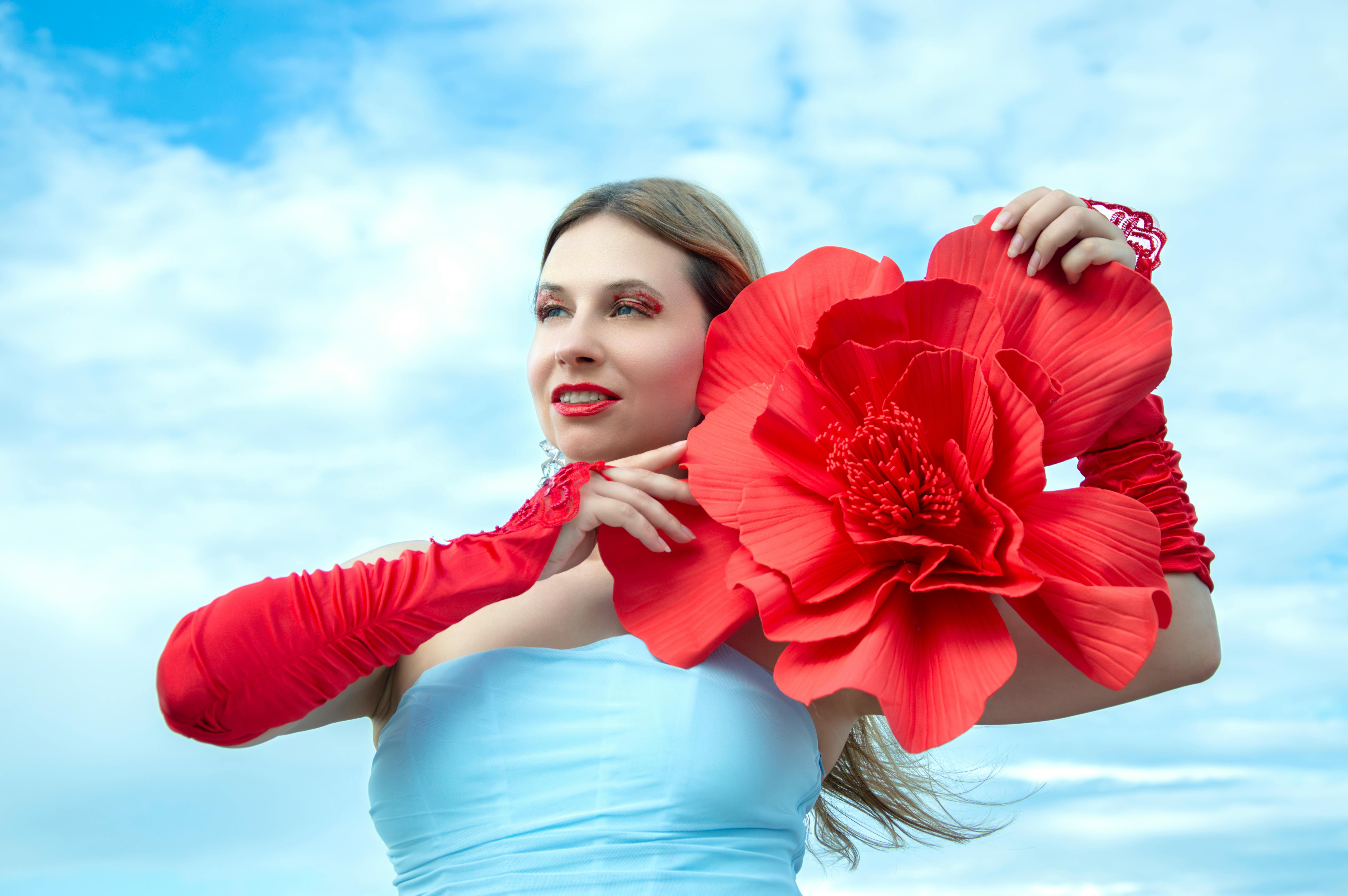 bezplatná Dospělá žena v červených rukavicích drží velký červený květ proti jasně modré obloze. Základová fotografie