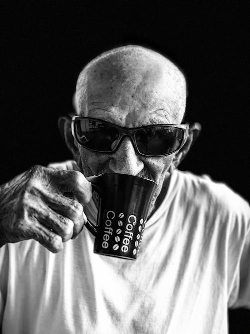 Homme En Chemise à Col Rond Blanc Portant Des Lunettes De Soleil Noires Tenant Une Tasse En Céramique Noire