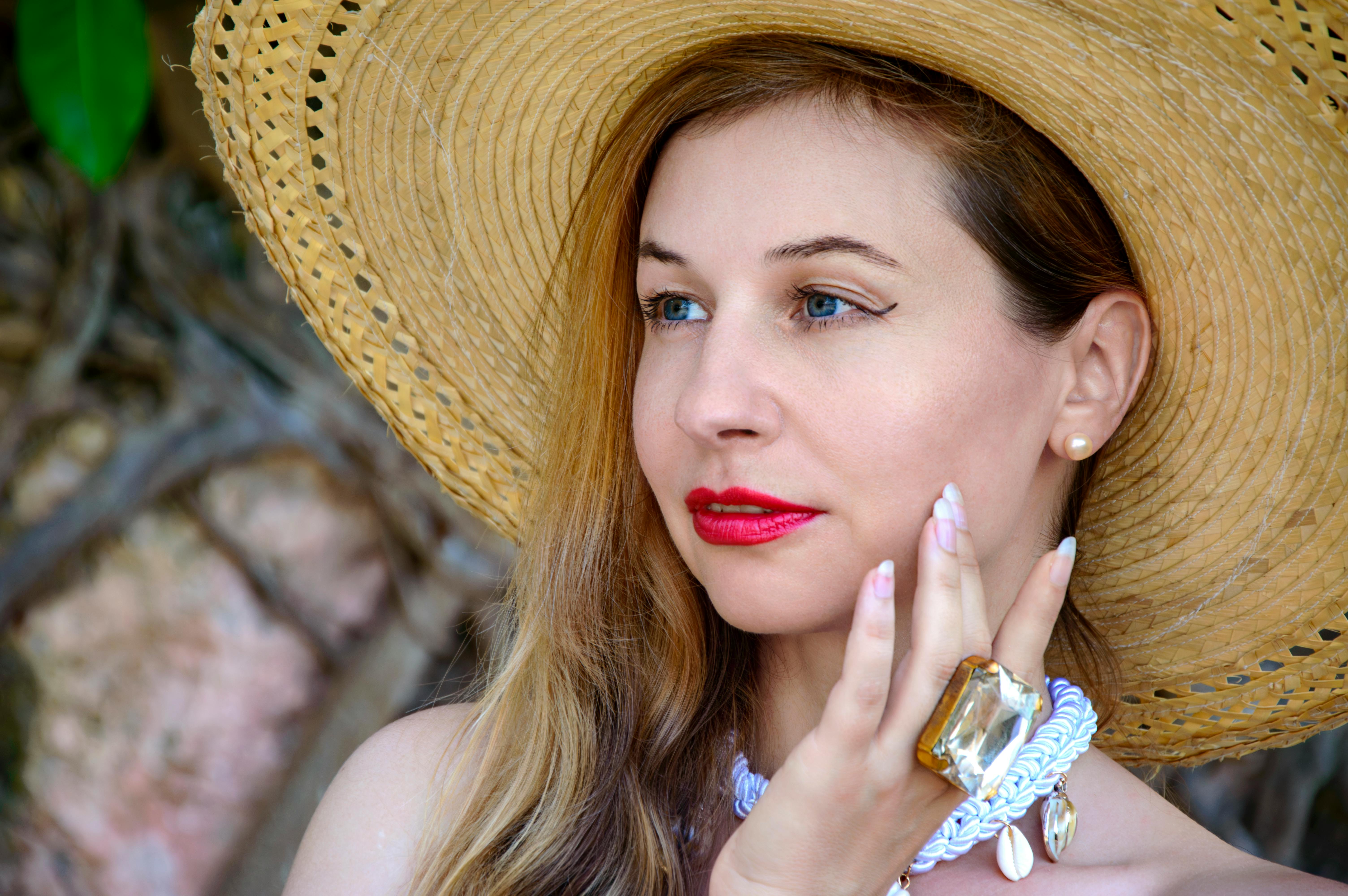 ฟรี ภาพระยะใกล้ของหญิงสาวสวมหมวกฟางและเครื่องประดับหรูหรา ทาลิปสติกสีแดงสด ในฉากหลังกลางแจ้ง คลังภาพถ่าย