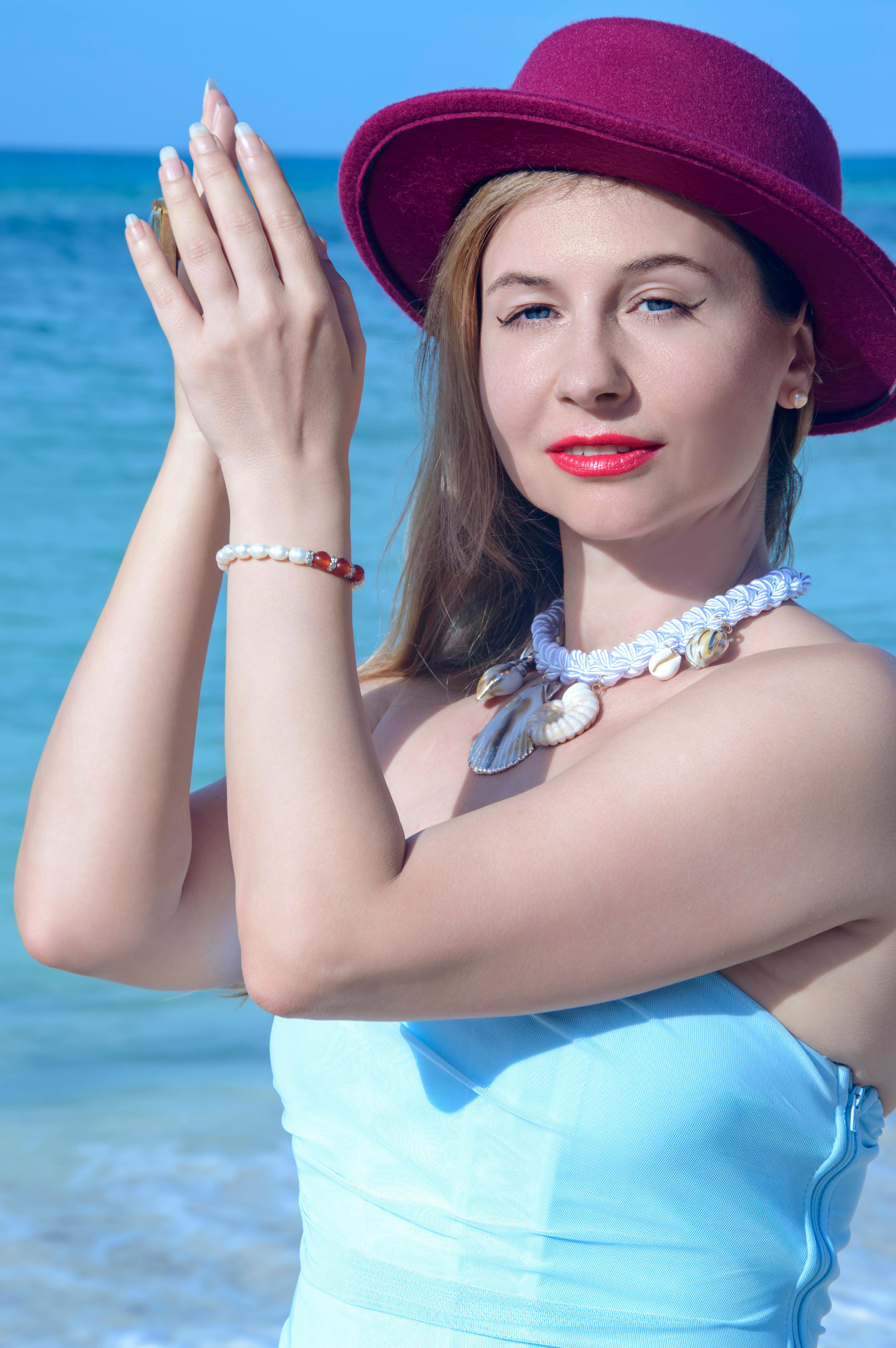 Gratis Donna elegante con un cappello rosso che si gode una giornata di sole in riva all'oceano. Foto a disposizione