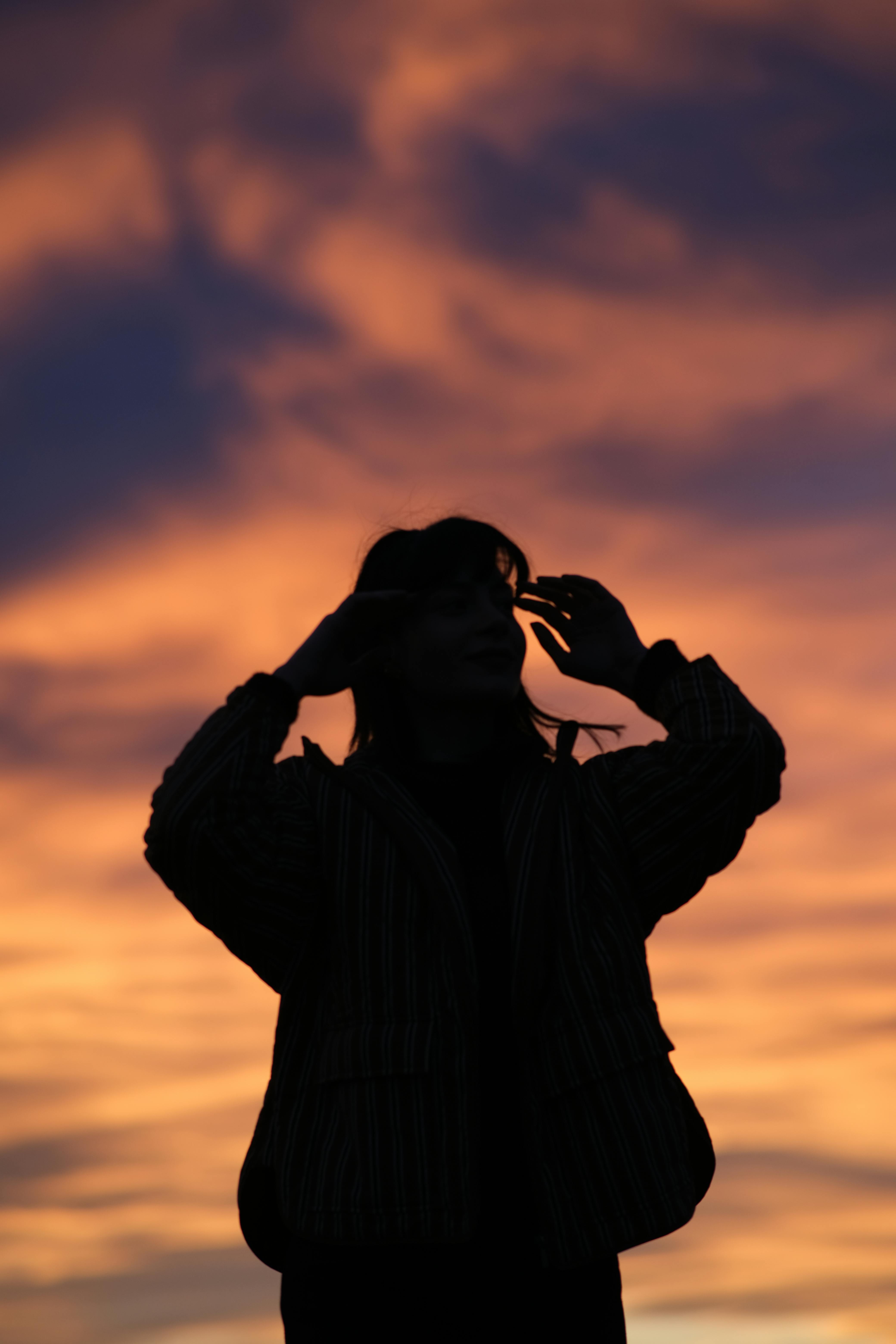 grátis Uma silhueta deslumbrante de uma pessoa sob um pôr do sol vibrante em tons de laranja e roxo, criando um efeito místico. Foto profissional