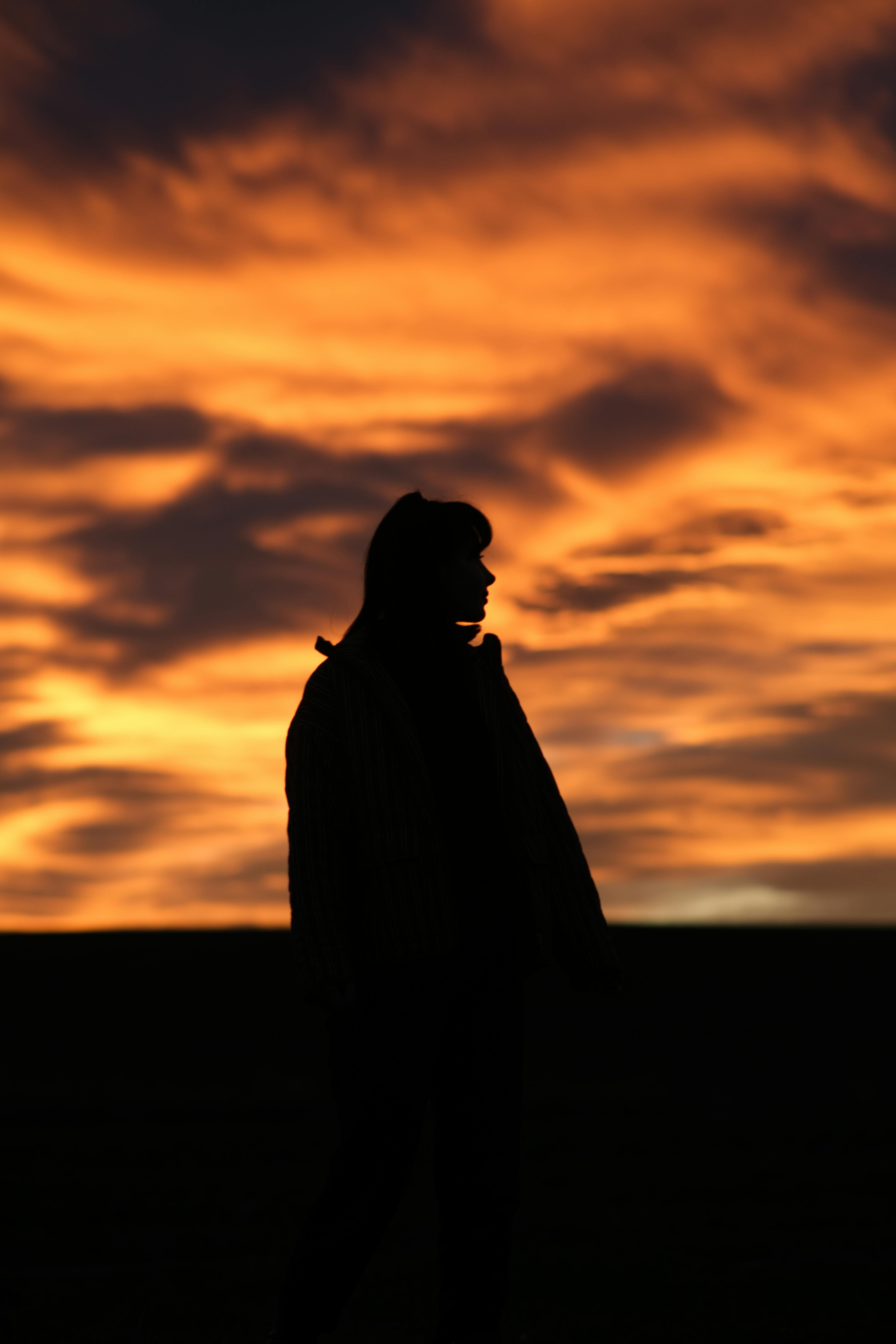 ฟรี ภาพเงาของคนคนหนึ่งตัดกับท้องฟ้าในยามพระอาทิตย์ตกดินที่งดงาม สร้างบรรยากาศที่ชวนให้รู้สึกถึงอารมณ์ต่างๆ คลังภาพถ่าย
