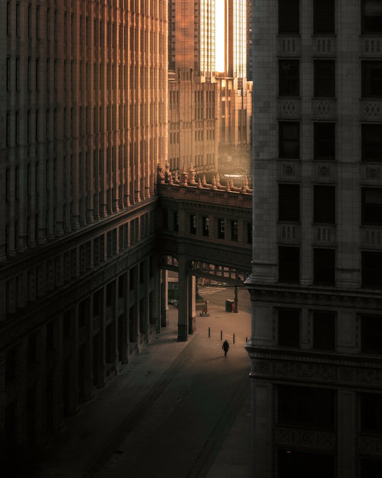 Person Walking On Street Between Buildings