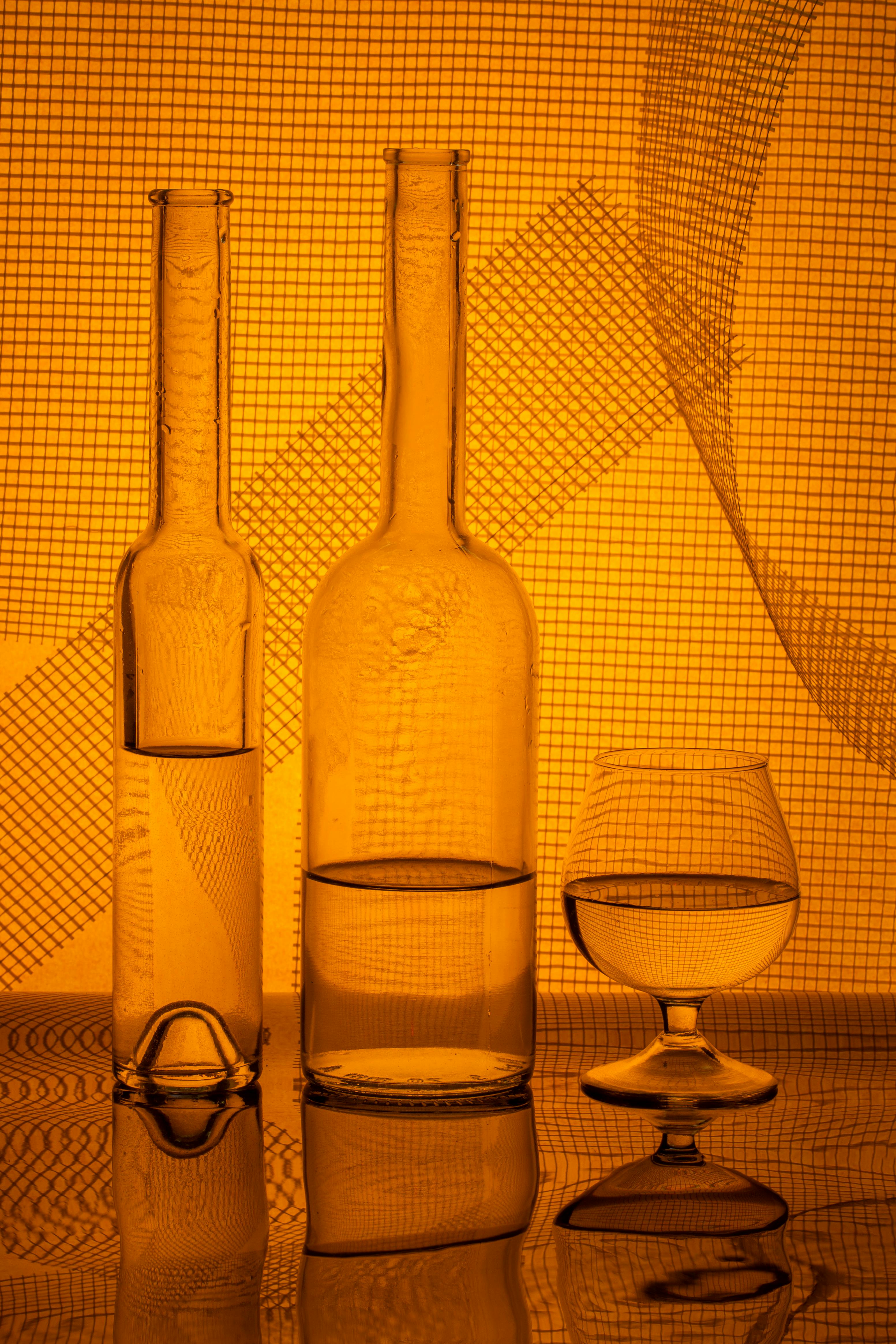 Bezpłatne Elegancka aranżacja szklanych butelek i kieliszka z abstrakcyjnym oświetleniem. Zdjęcie z galerii