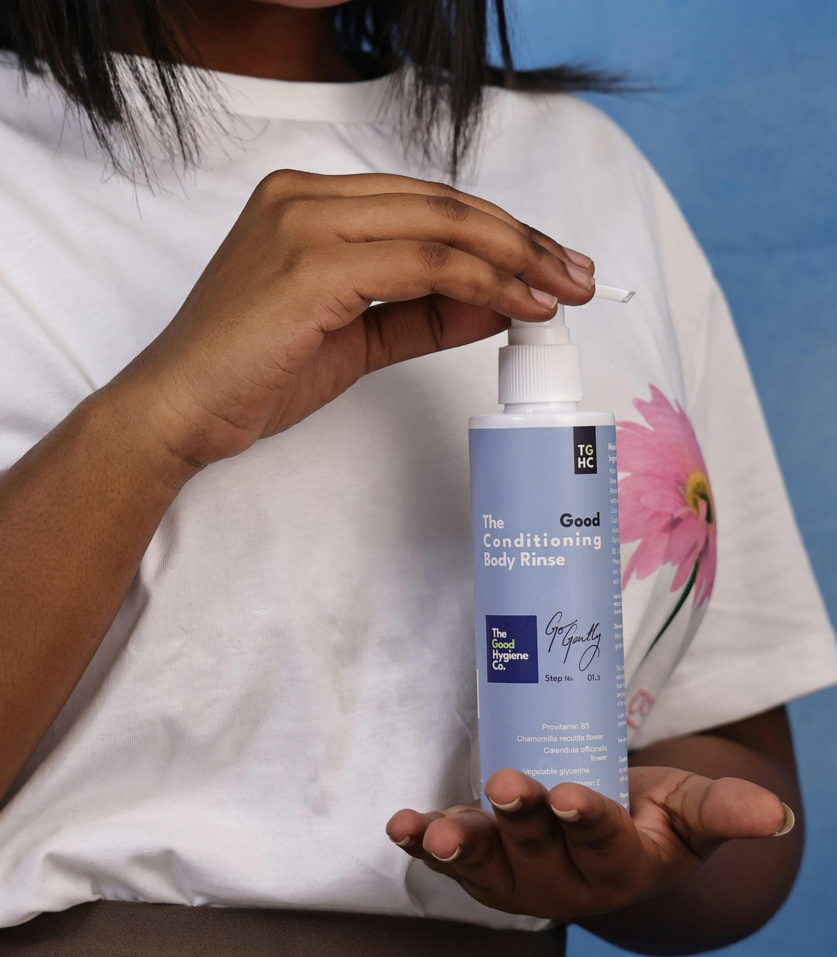 Ilmainen Lähikuva naisesta levittämässä hoitoainetta vartalolle sinisestä pullosta sisätiloissa. Kuvapankkikuva