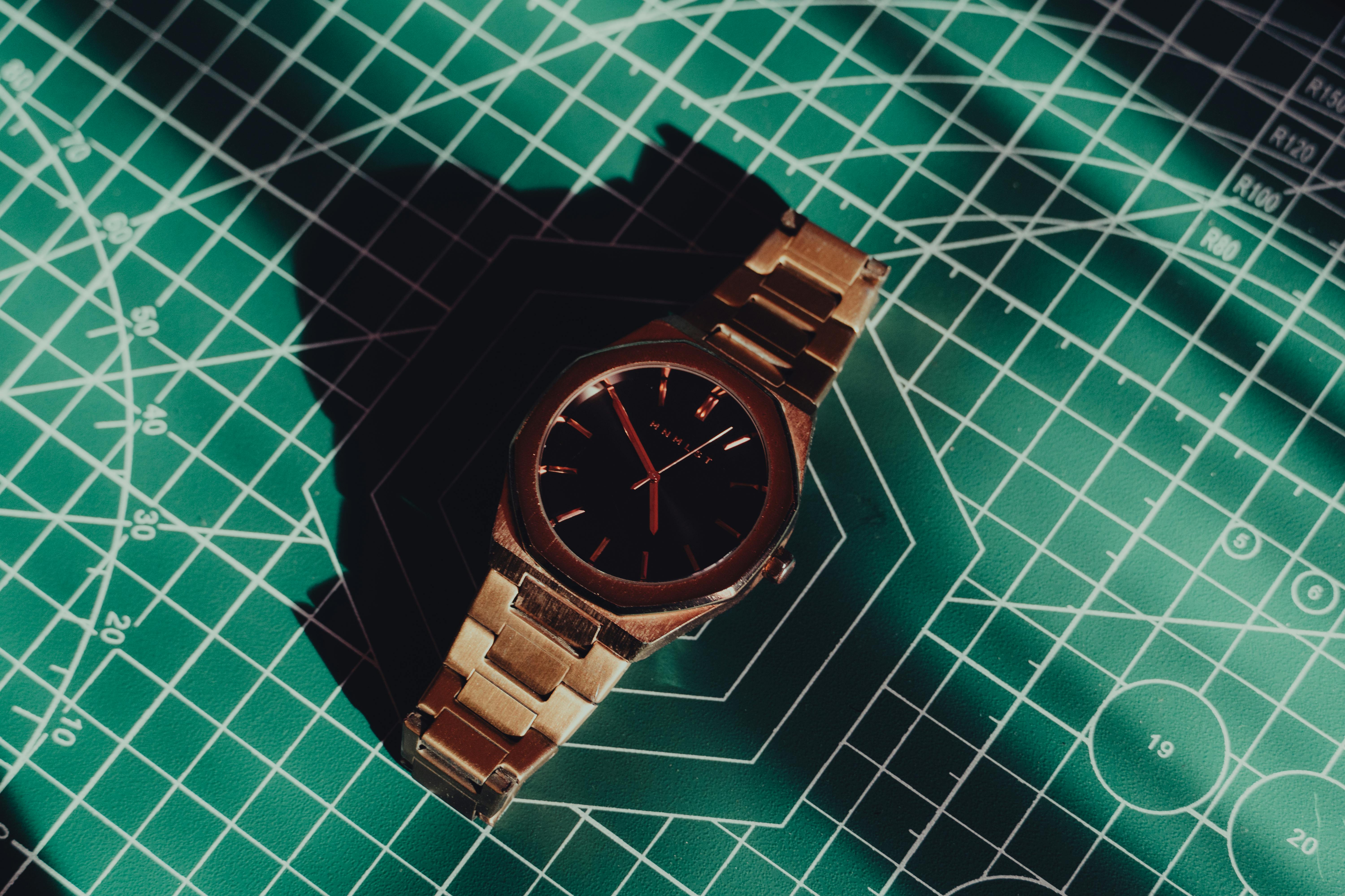 Gratis Un reloj clásico presentado sobre un tapete geométrico con sombras que resaltan su elegancia. Foto de stock