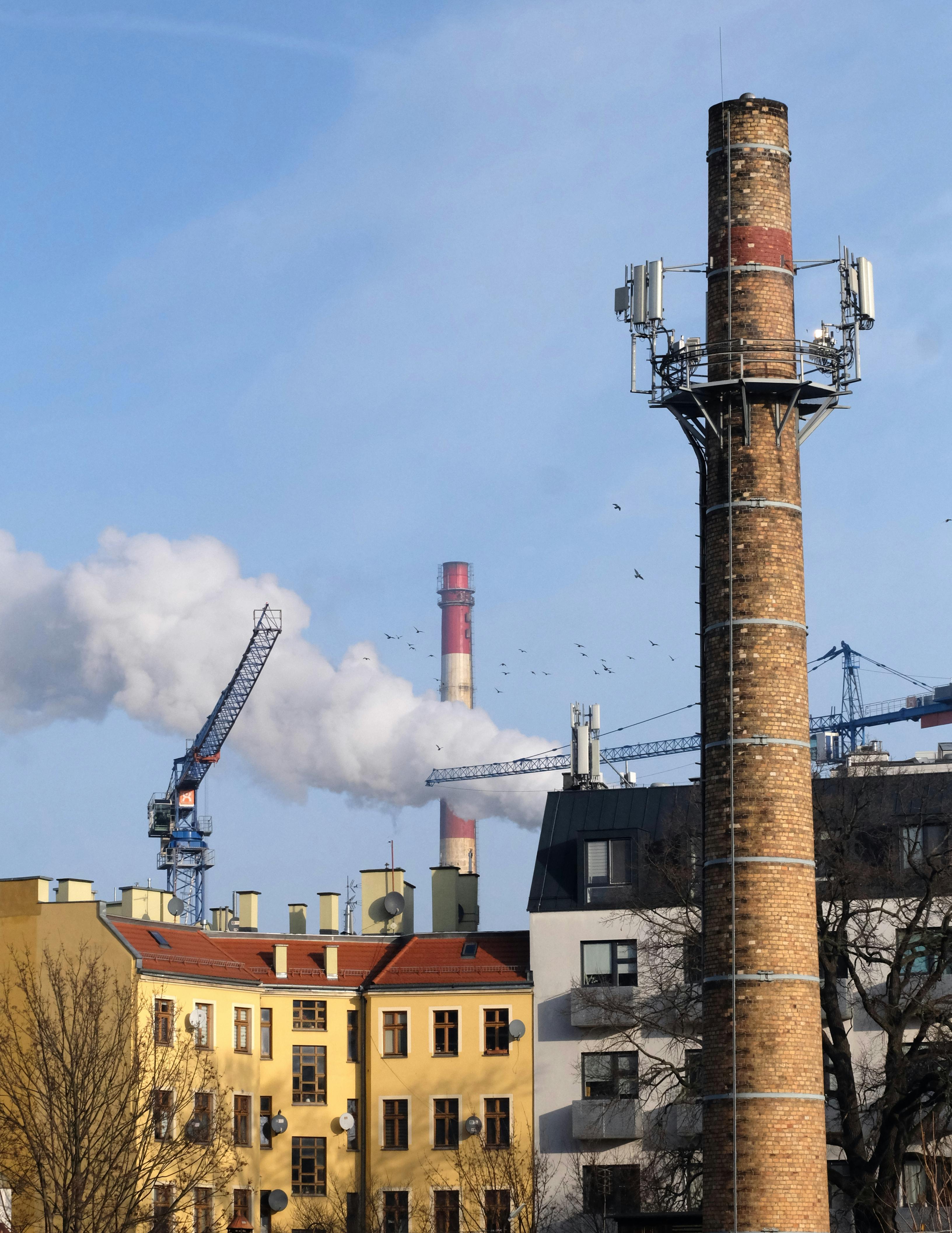 bezplatná Městská scéna s komíny a jeřáby pod jasnou modrou oblohou, představující průmyslovou architekturu. Základová fotografie