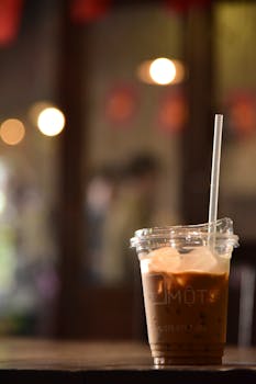 Chilled iced coffee in a plastic cup on a wooden table, perfect for a refreshing break in a cozy café.
