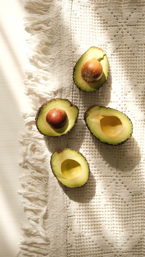 Free Sliced avocado halves on a sunlit textured fabric capturing natural light and organic elements. Stock Photo