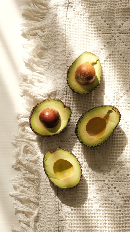 Free Sunlit avocados halved on a woven fabric backdrop create a natural, healthy vibe. Stock Photo