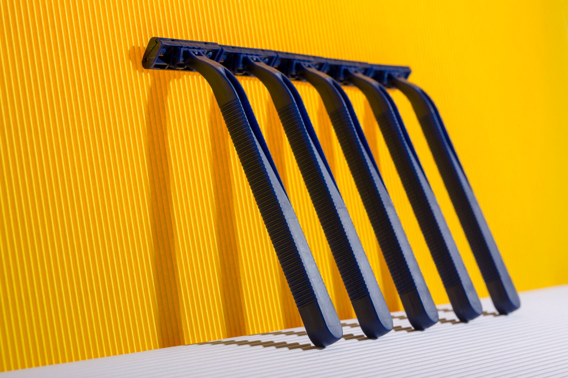 Five blue razors aligned against a vibrant yellow background creating a bold visual contrast.