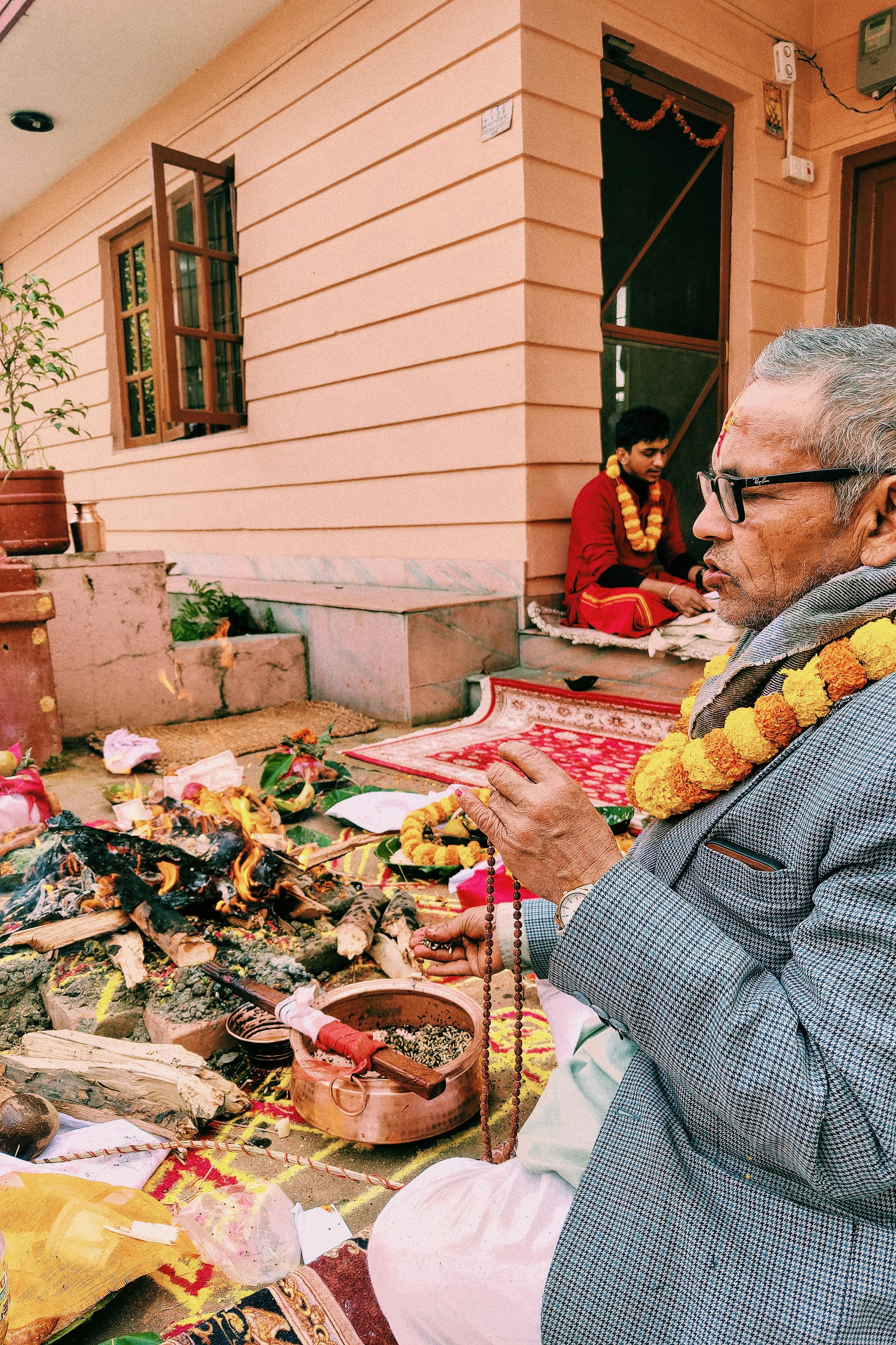 Elderly man performing a Hindu ritual ceremony with offerings, prayers, and fire.