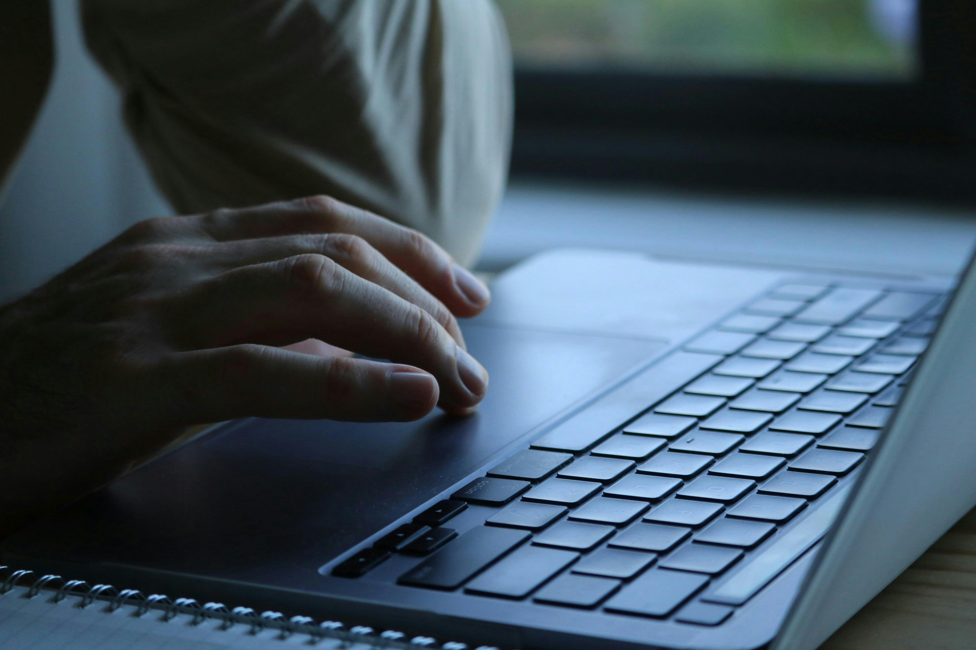 Close-up of a person's hands typing on a laptop keyboard indoors. Soft lighting.