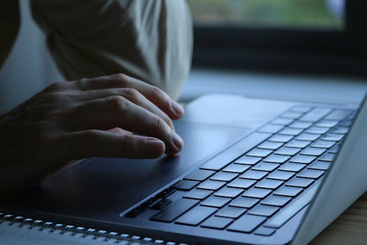 Close-up of a person's hands typing on a laptop keyboard indoors. Soft lighting.