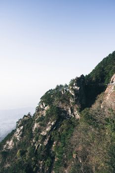 A breathtaking view of a rugged rocky mountainside adorned with green trees under clear blue skies.