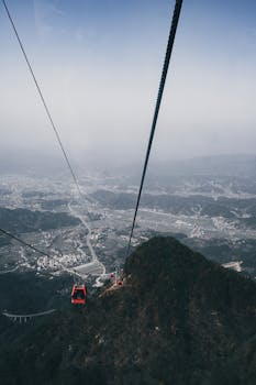 A breathtaking aerial view of a cable car over a mountainous landscape with a sprawling city in the distance.