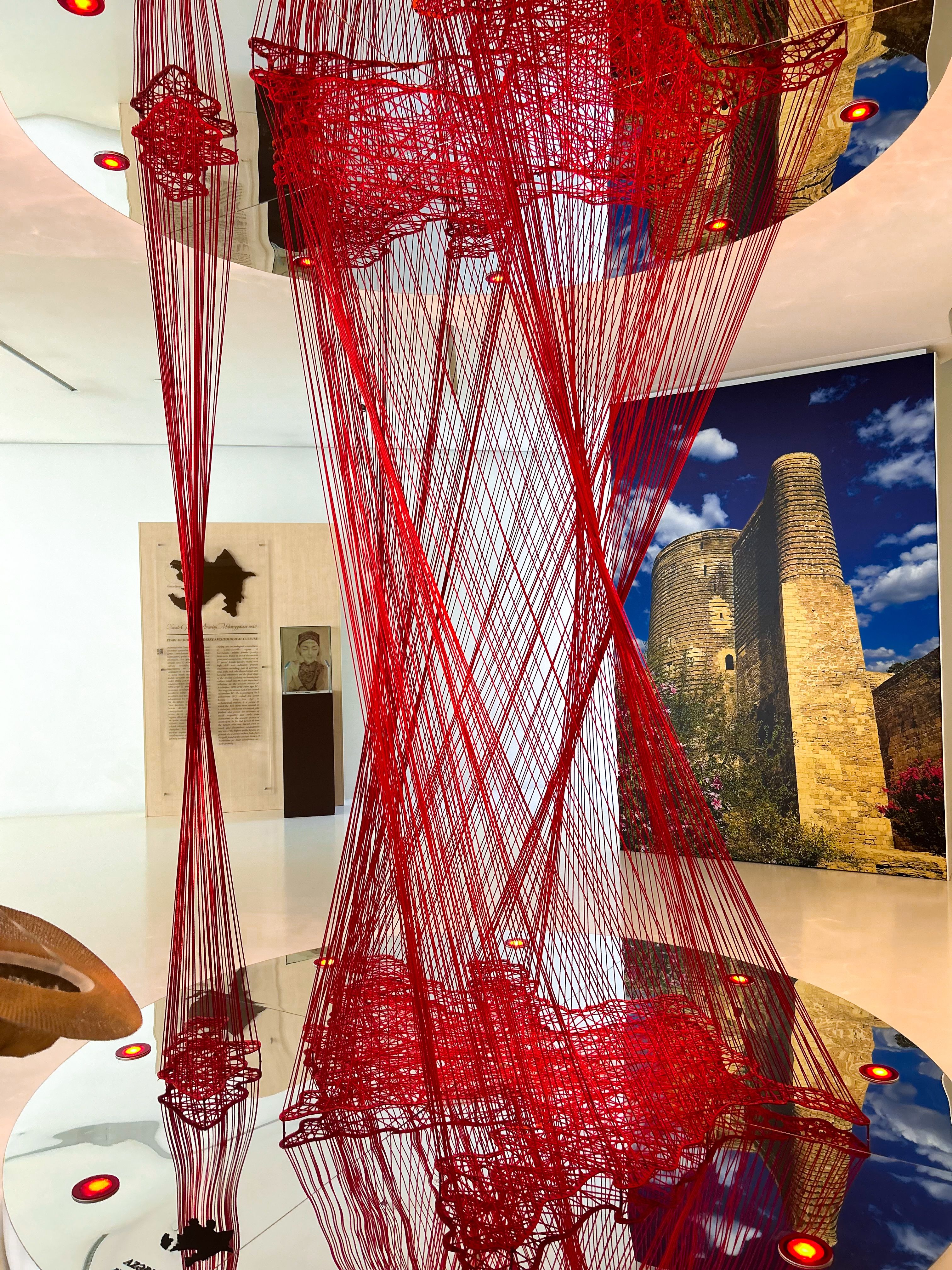 Free Innovative art featuring red strings with historic tower backdrop at a gallery in Baku. Stock Photo
