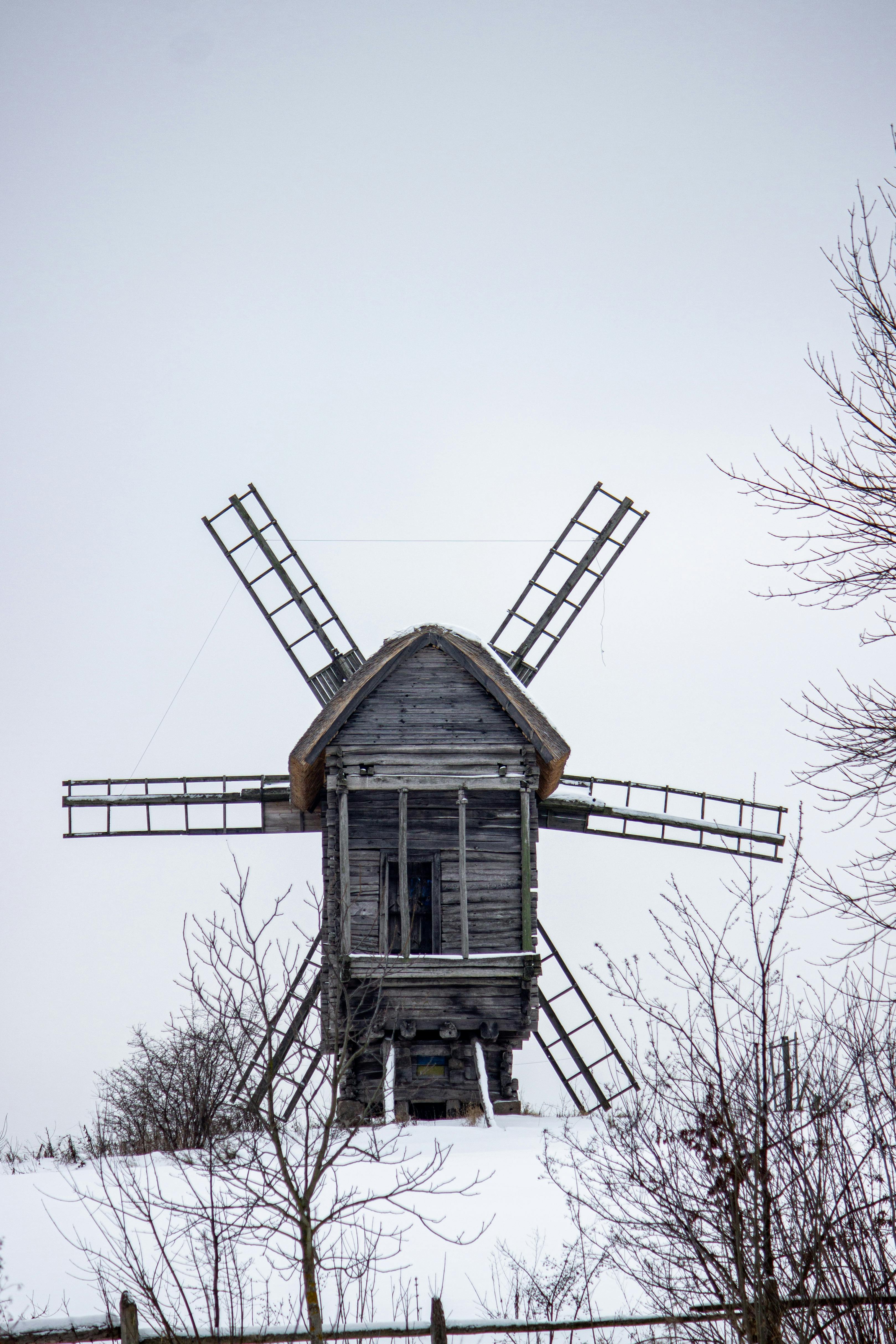 ฟรี กังหันลมไม้เก่าแก่ที่สวยงามตั้งอยู่บนเนินเขาที่ปกคลุมด้วยหิมะ ล้อมรอบด้วยต้นไม้ในฤดูหนาว คลังภาพถ่าย