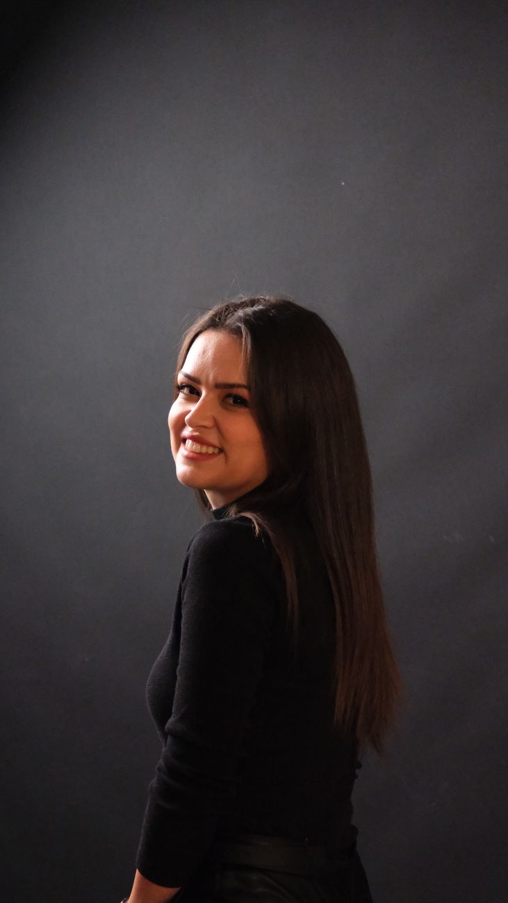 Studio portrait of a smiling woman in Ankara, captured with a dark background and soft lighting.