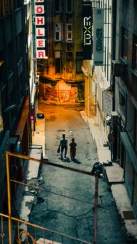 Two people walking down a dimly lit urban alleyway at night.