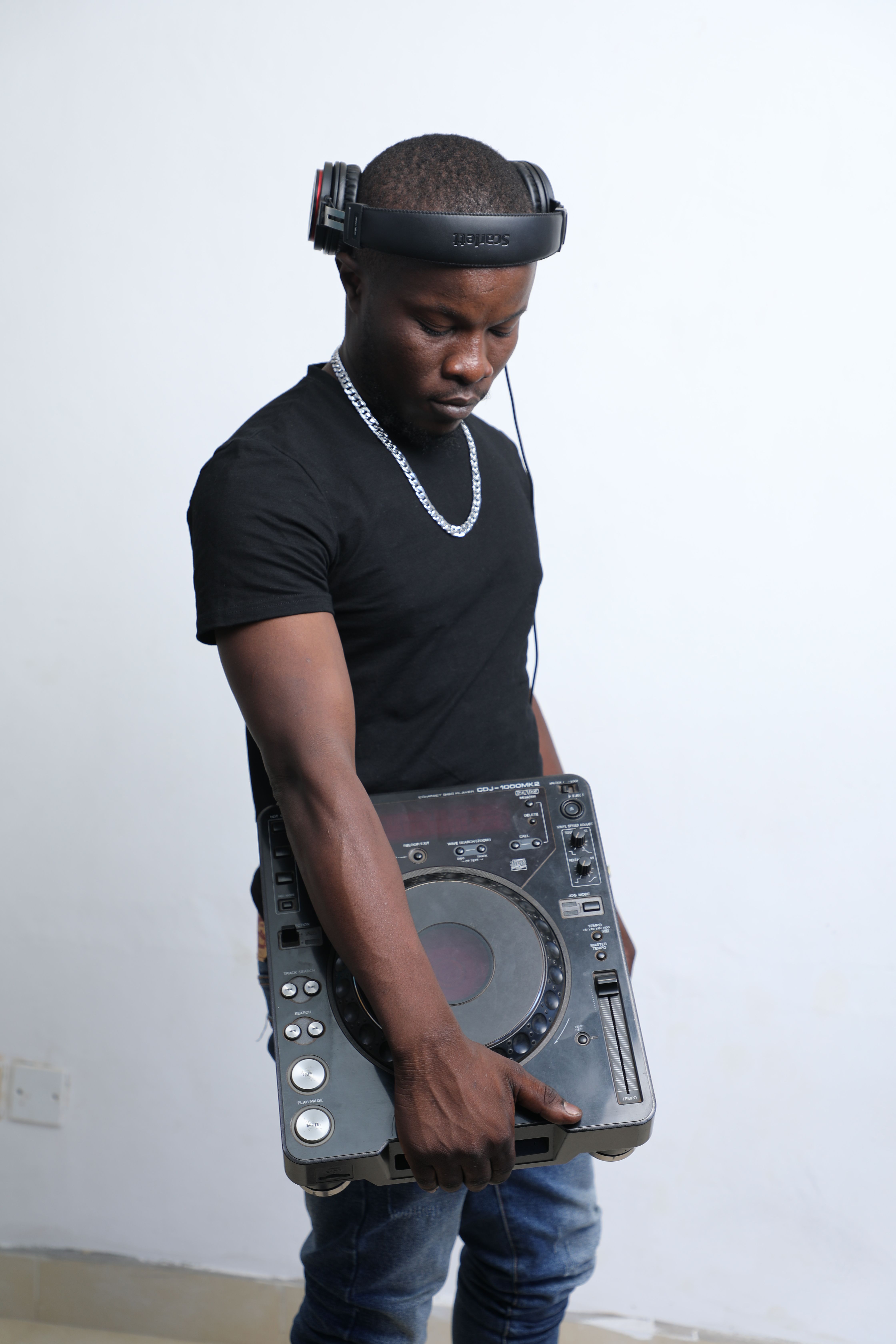 Young DJ wearing headphones and holding a mixer in a studio setting.
