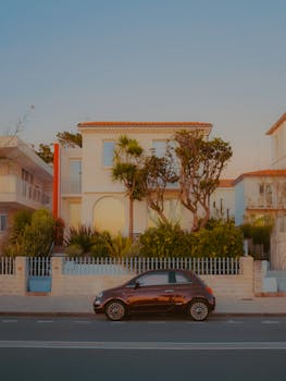 A stylish Mediterranean-style house with palm trees and parked car at sunset.