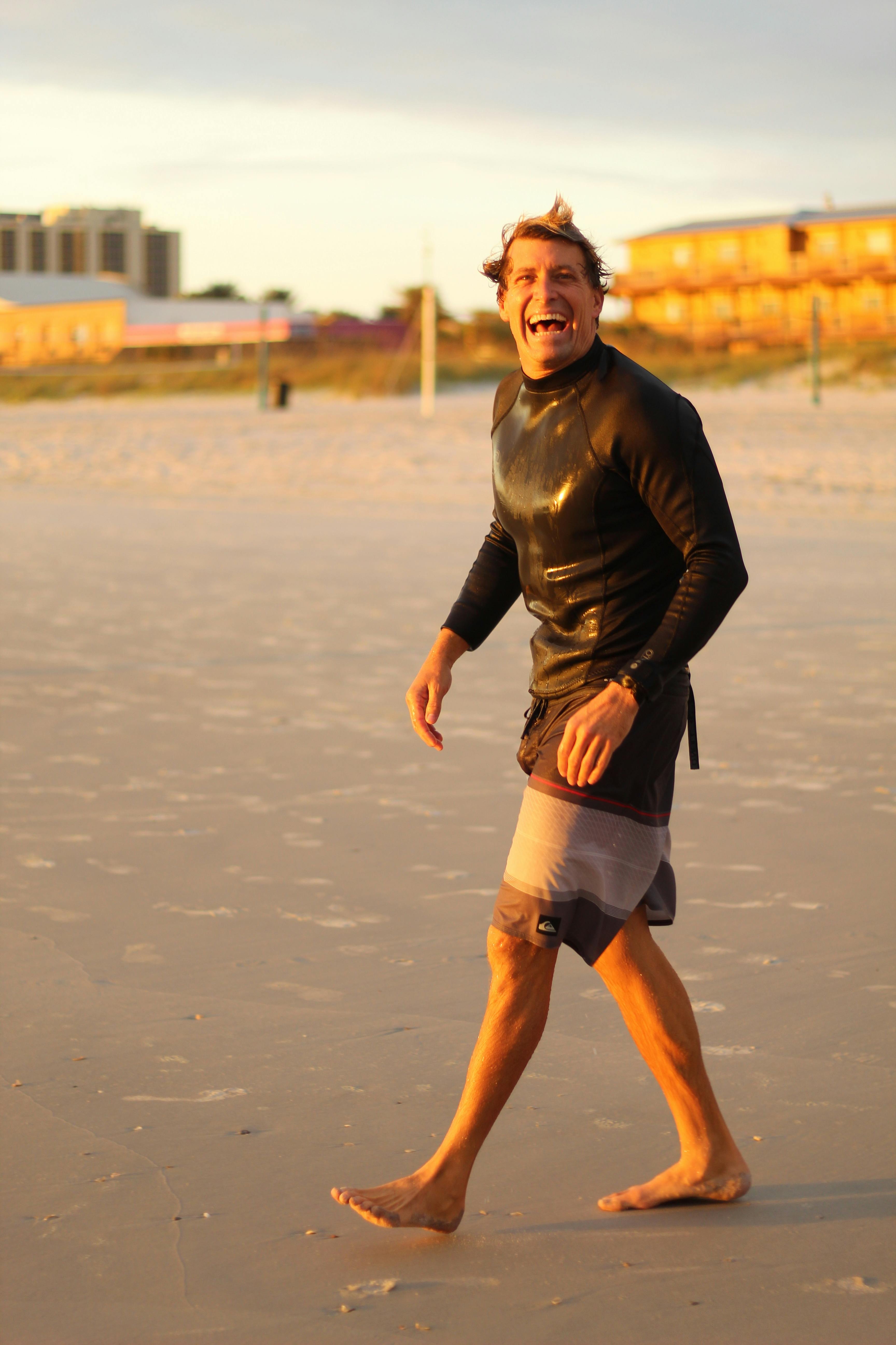 一位快乐的冲浪者穿着潜水衣，赤脚走在海滩上，享受着夏日时光