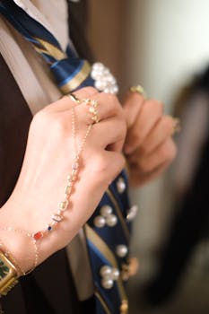 Close-up of hands wearing jewelry and adjusting a pearl-accented tie.